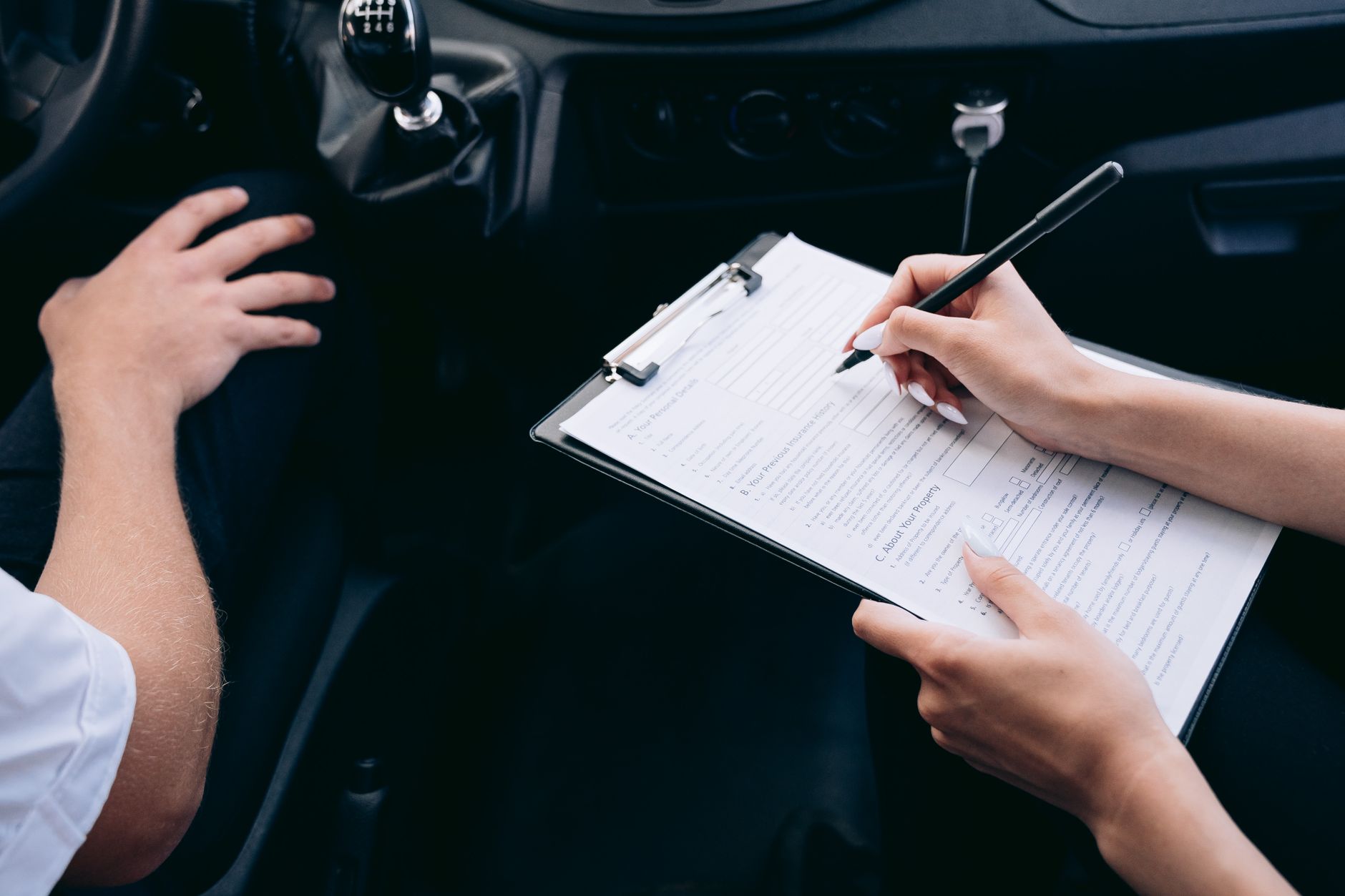 車内でクリップボードに挟んだ保険の申込書に記入している人の手元