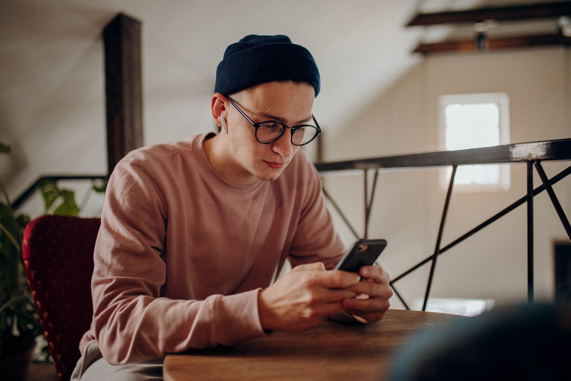 自宅のテーブルで、ニット帽と眼鏡の男性が手に持ったスマートフォンの画面を見ている