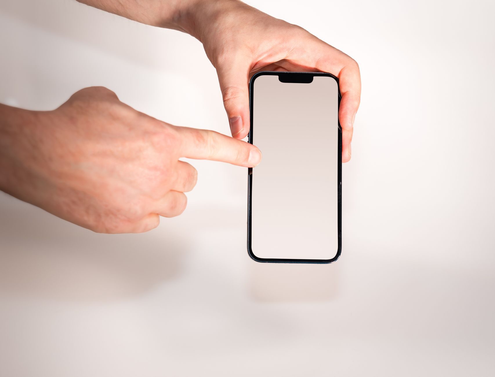 何も表示されていないスマートフォンの画面を指で押そうとしている手元
