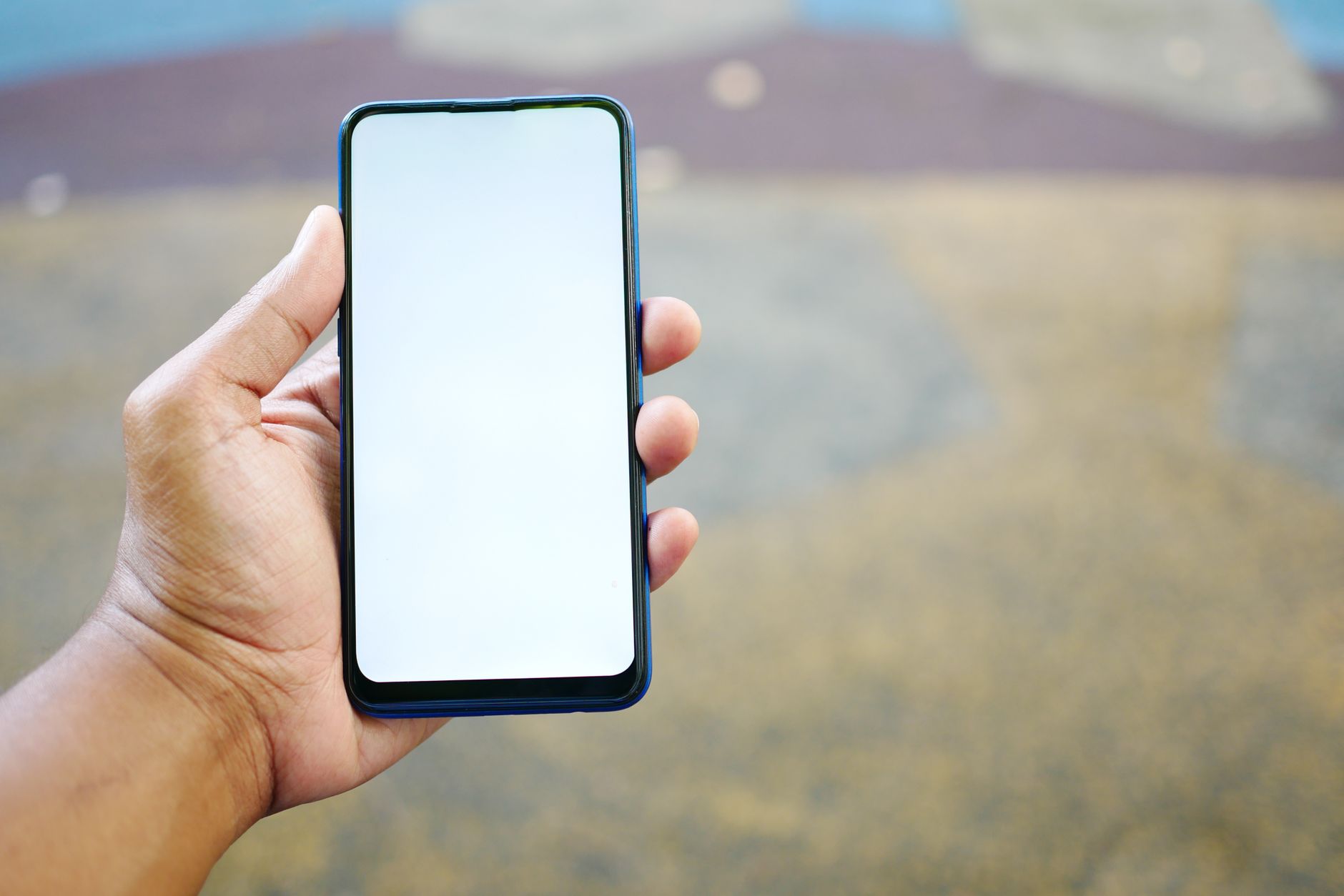 屋外で、画面が真っ白な青いスマートフォンを片手で持っている手元のクローズアップ