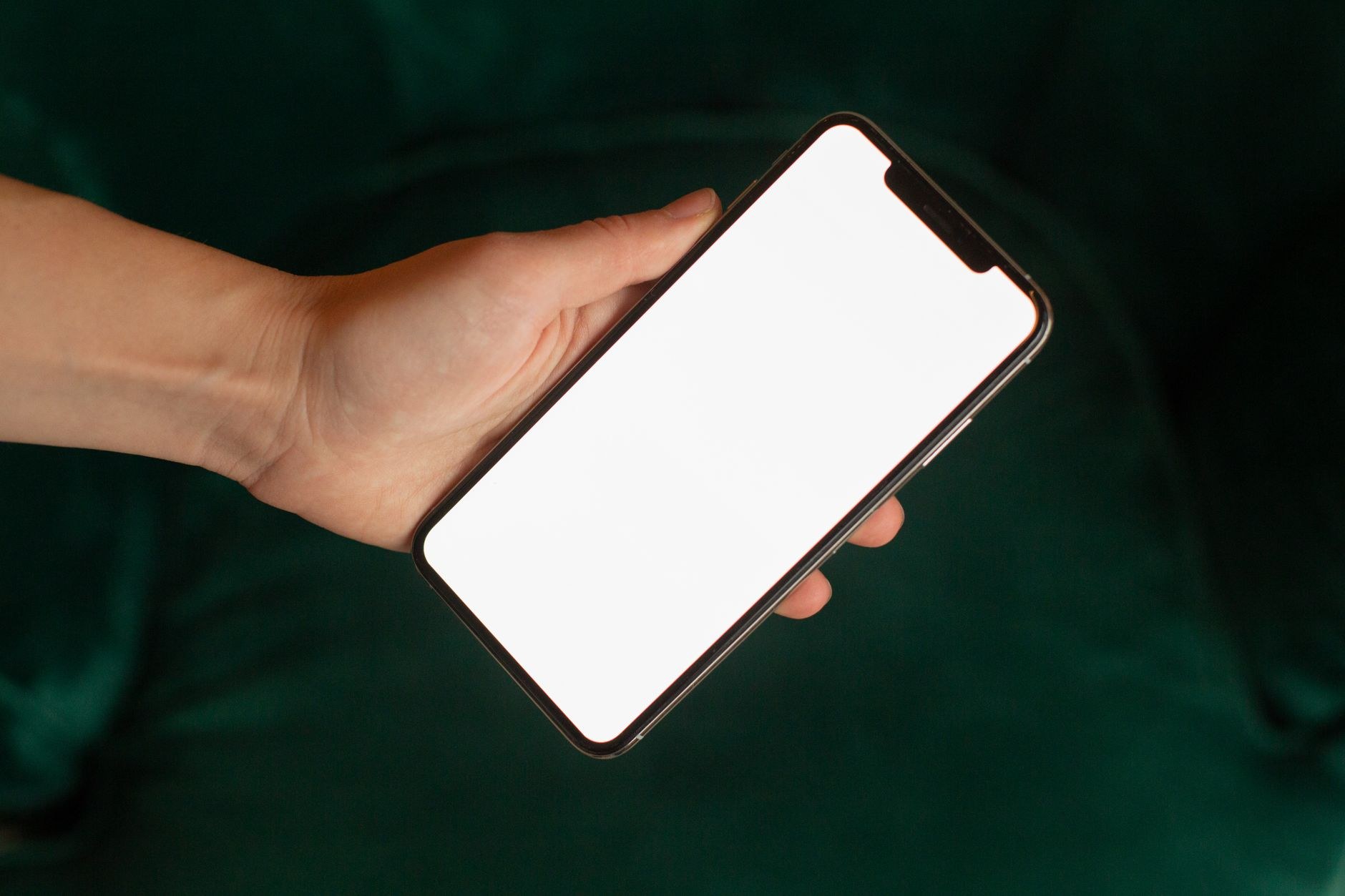 暗い緑色の背景で、画面が白いままのスマートフォンを片手で持っている様子